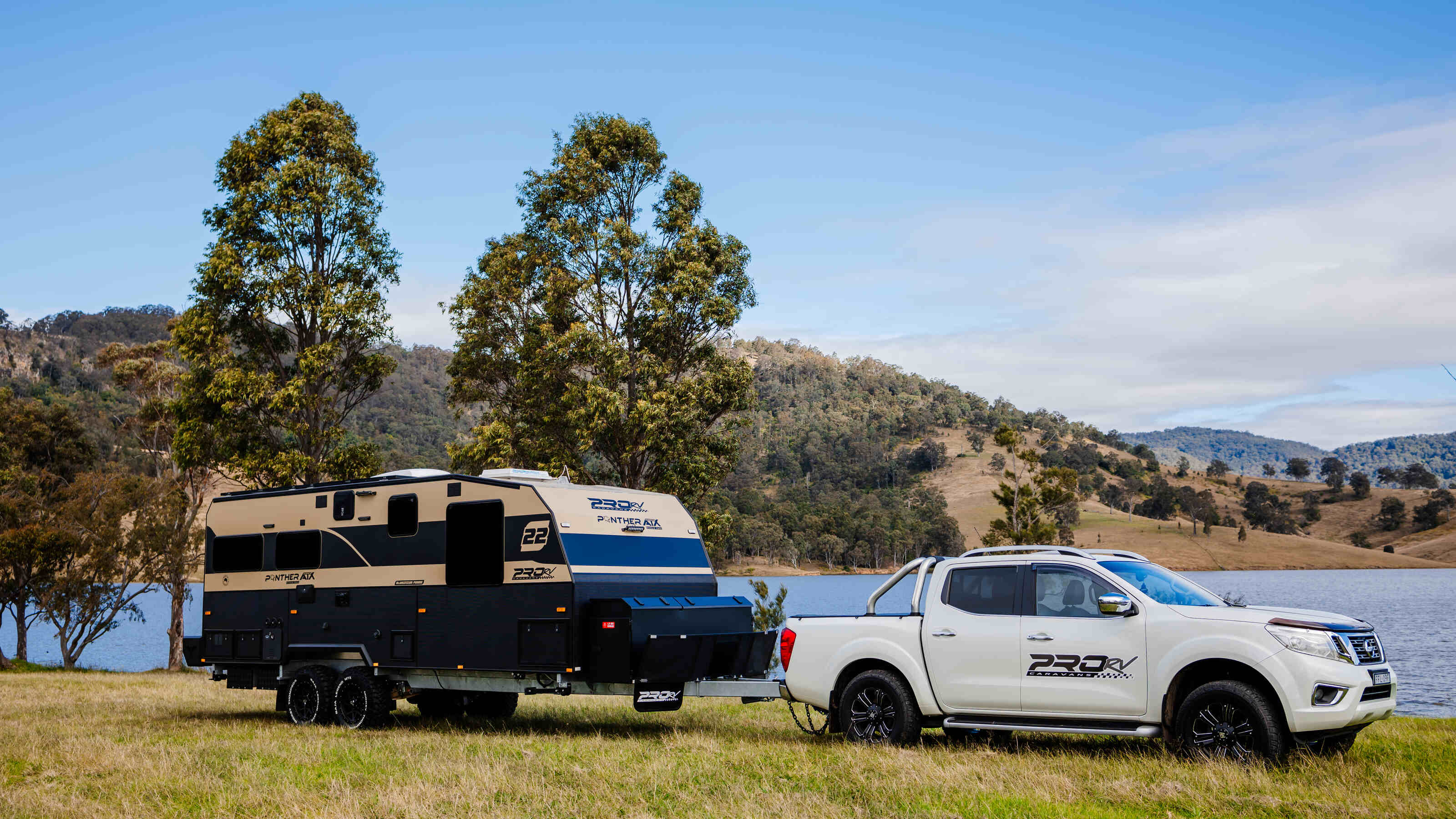 PRORV Caravans Panther caravan attached to a utility vehicle near a lake.